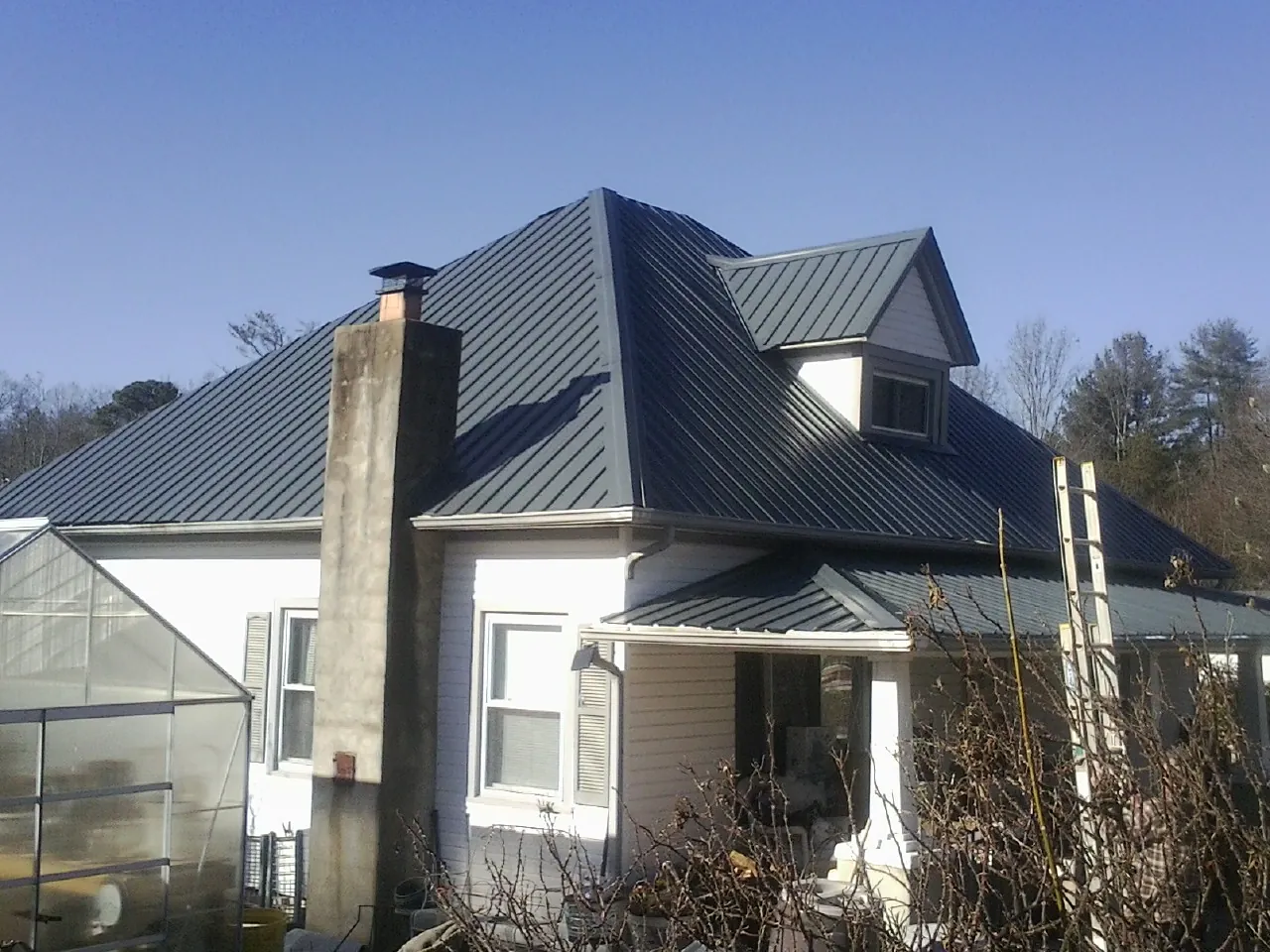 Dark blue standing seam metal roof on a white farmhouse with dormer — Slate & Tile Roof Repair by Roofing Brothers in Grand River