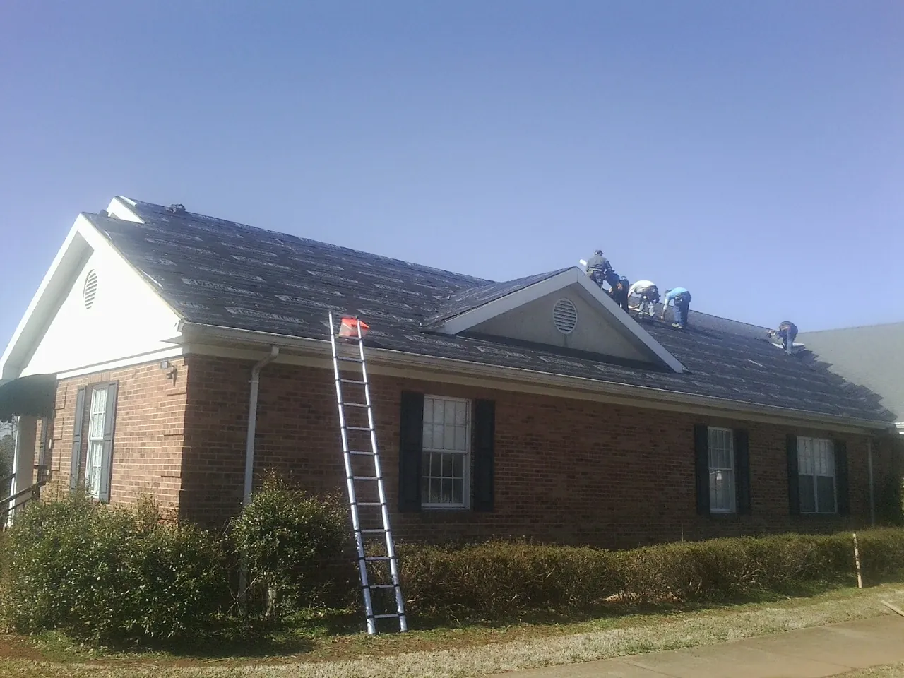 Crew tearing shingles off a brick ranch roof with a ladder set — Metal Roof Repair work by our crew in Grand River