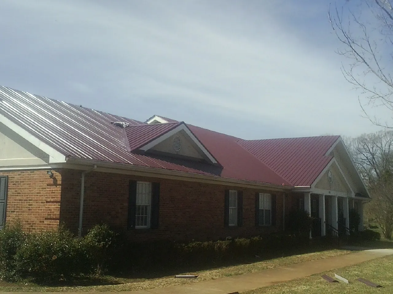 Red metal roof with gabled entries on a long brick building, from a Hail Damage Roof Repair job in Grand River