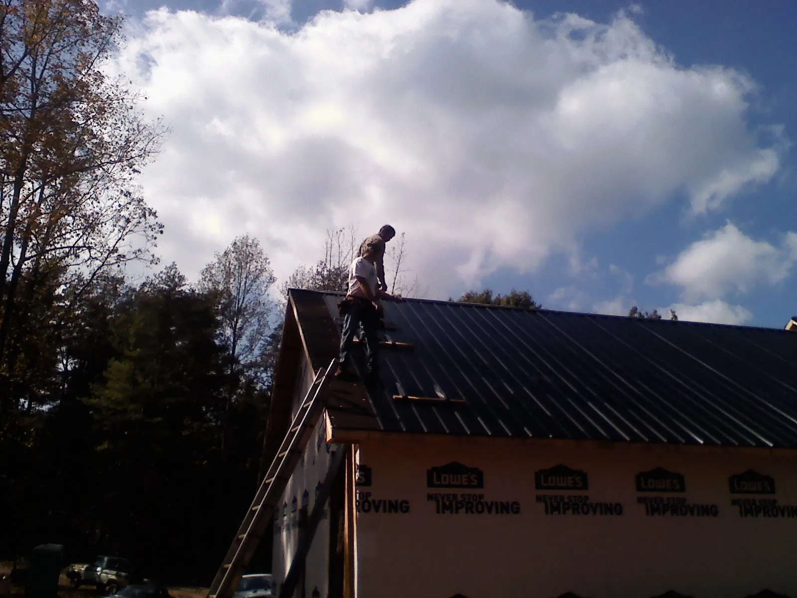 Roofer fastening dark metal panels high against a cloudy sky, from a Roof Inspection job in Grand River