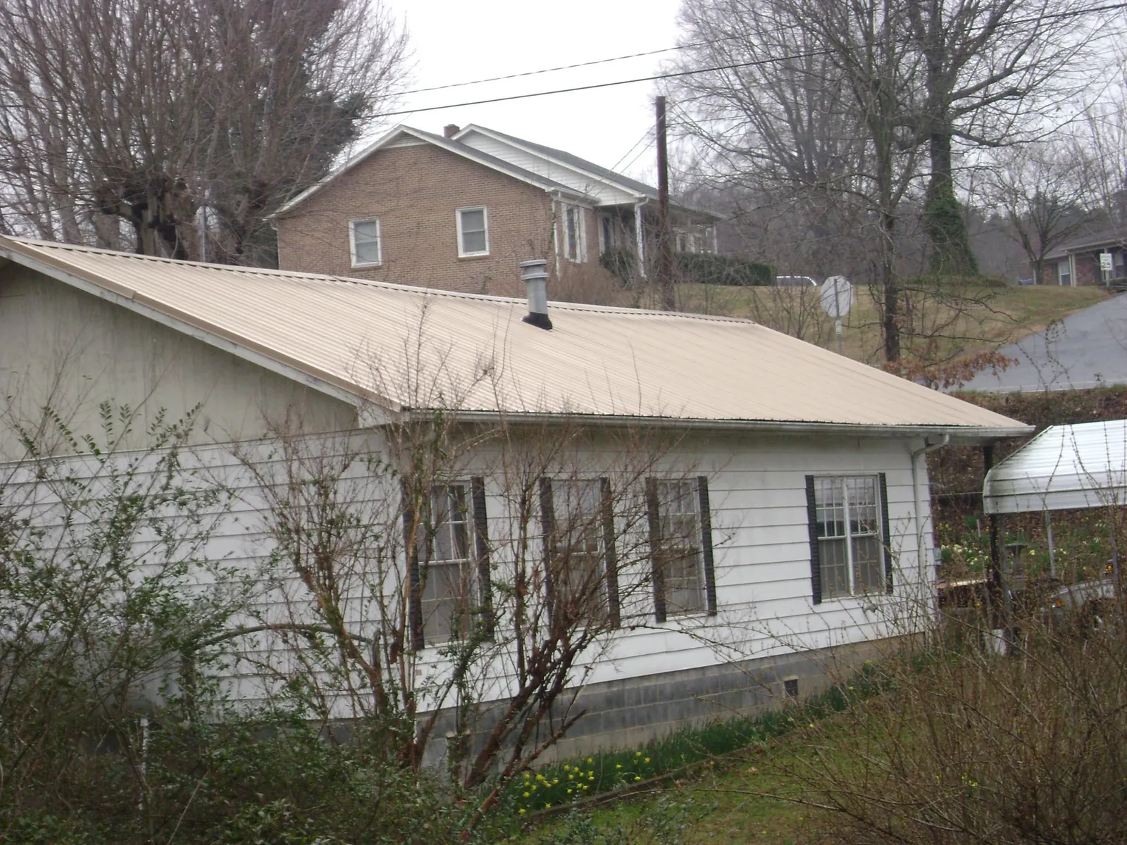 Tan metal roof on a white sided house set into a hillside — Commercial Roofing by Roofing Brothers in Grand River