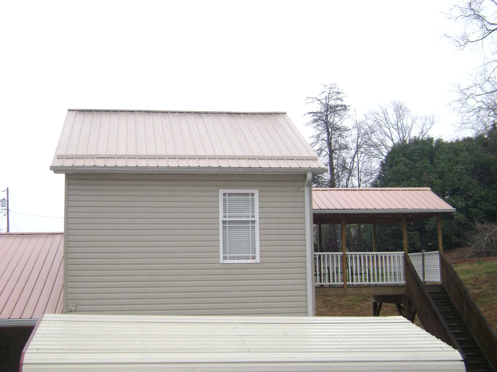 Tan metal roofs on a two story addition and attached porch, from a Roof Replacement job in Grand River